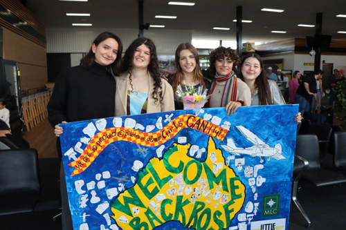 Rose's friends welcome her at the airport with a sign made by Junior School students.